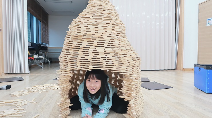 목재칩으로 만든 원형 탑 속에서 장난스럽게 웃으며 브이를 하고 있는 참가자 가족의 모습