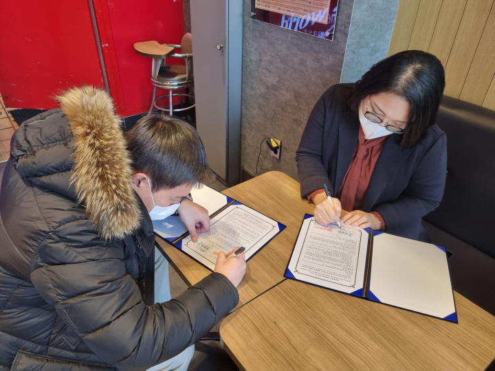 명도복지관 최미진관장님과 롯데리아 목포용해점 지점장님이 하나가게 협약서에 서명을 하고 있는 모습의 사진입니다