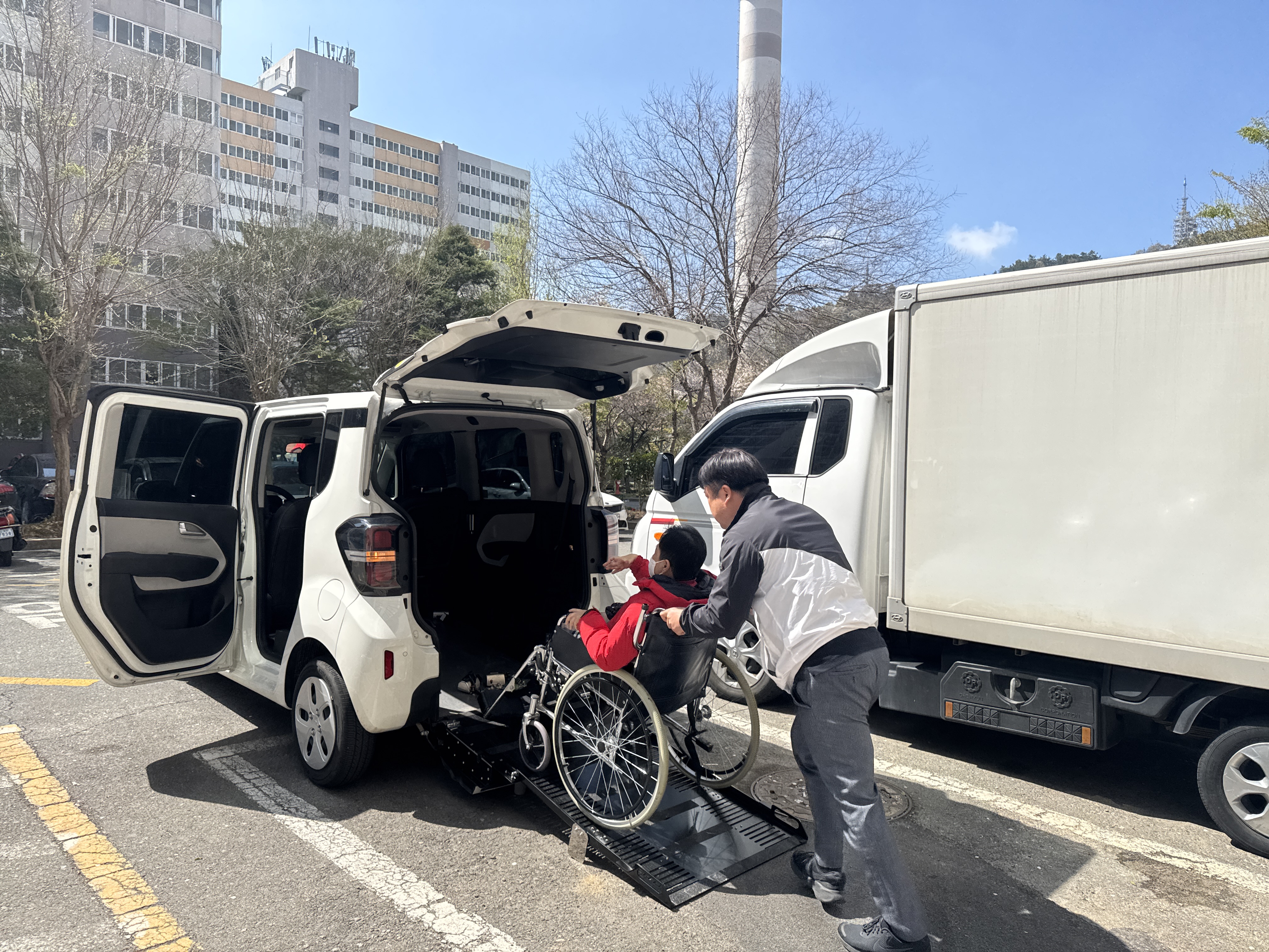 휠체어를 탄 이용인을 리프트카에 태우고 있는 담당 사회복지사의 사진입니다. 