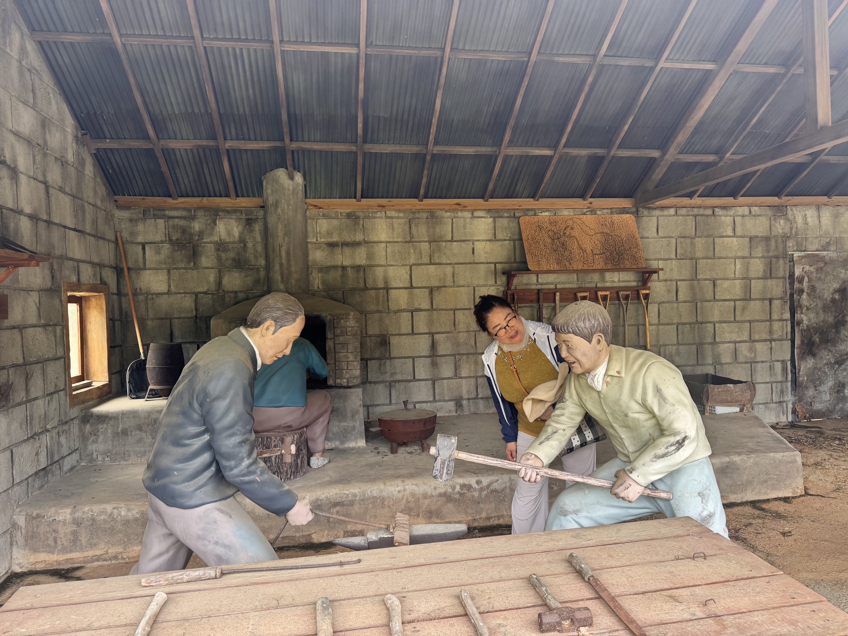 무안전통생활문화테마파크에서 모형으로 된 대장장이 전시물 앞에서 대장장이를 쳐다보고 있는 여성 재가장애인분의 사진입니다. 