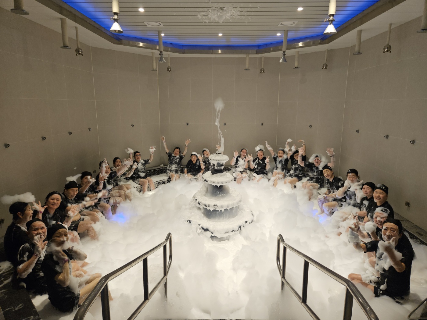 해조류거품 체험관에서 다함에 카메라를 응시하며 찍은 단체사진입니다. 해당 체험관에는 흰색 거품이 가득 채워져 있고, 자원봉사자들도 얼굴과 몸에 거품을 뭍히고 찍은 사진입니다. 