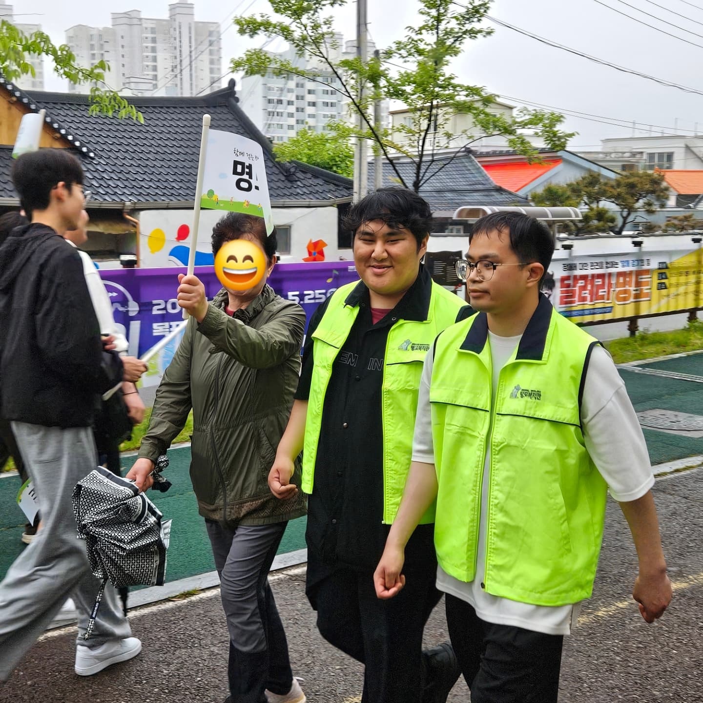'명도'라고 적힌 깃발을 든 지역주민과 자원봉사자, 장애당사자가 함께 걷고 있는 모습의 사진입니다.