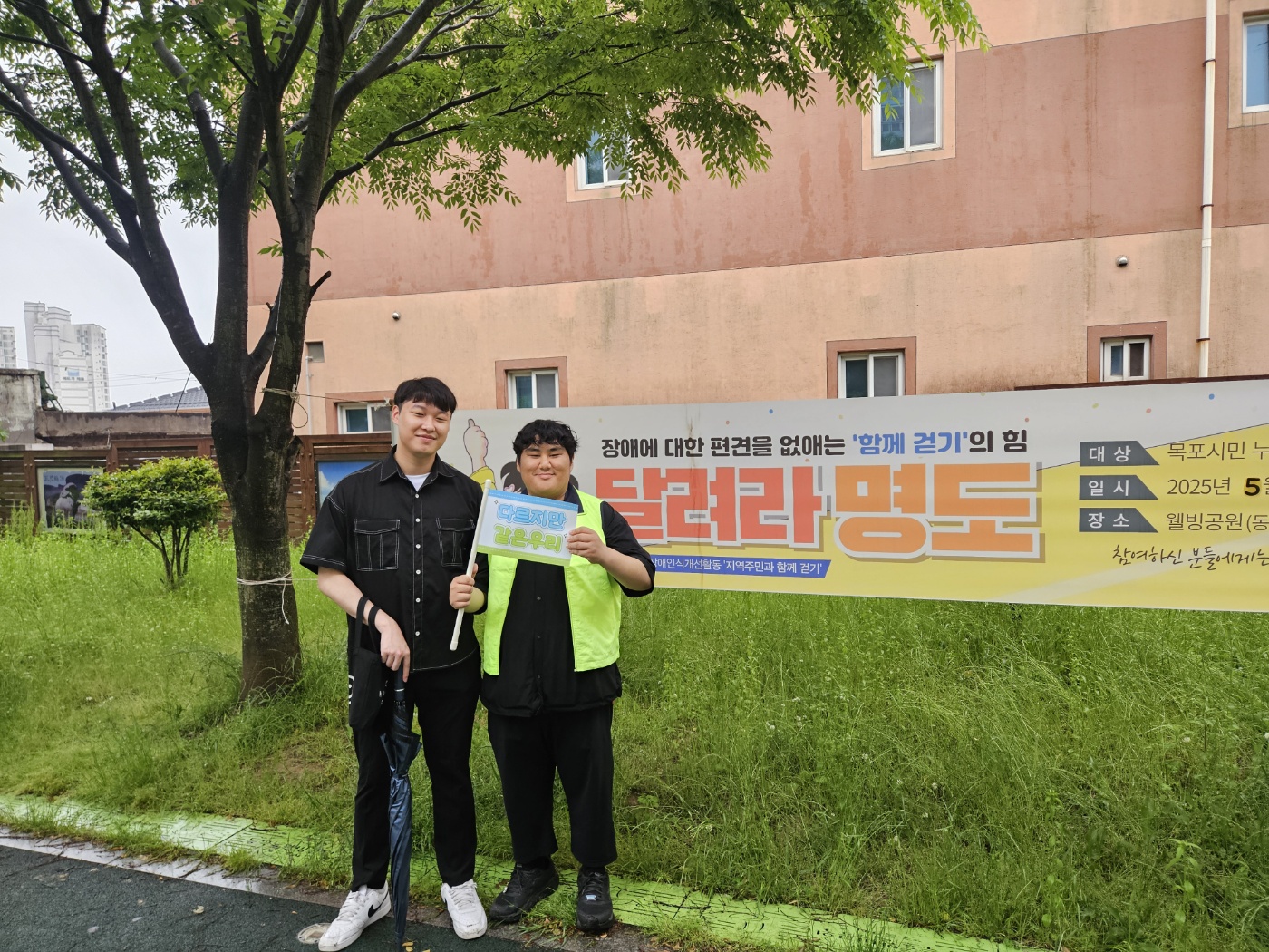 '달려라명도' 앞에서 '다르지만 같은우리'라고 적힌 깃발을 들고 지역주민과 자원봉사자가 함께 찍은 사진입니다.