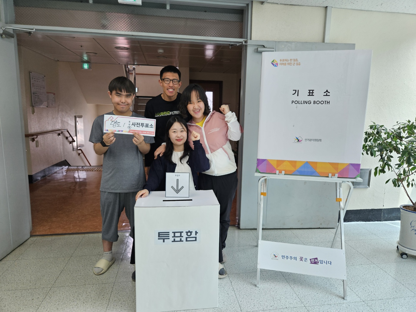 투표함과 기표소를 배경으로 이용인 세명과 사회복지가 함께 찍은 기념사진입니다. 