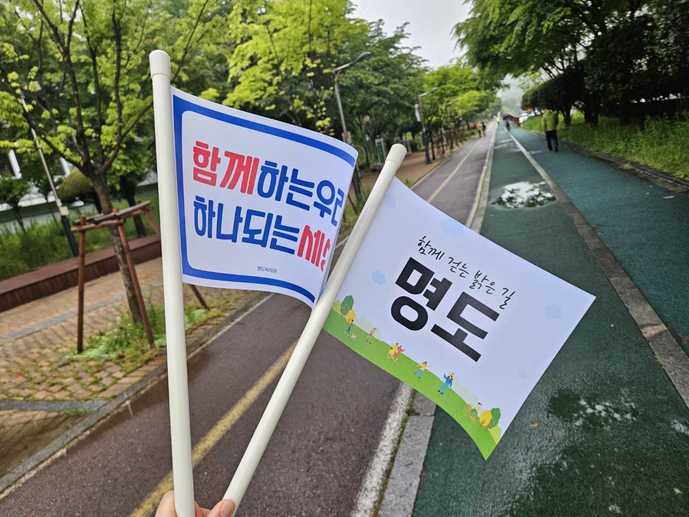 '함께하는 우리, 하나되는 세상', '함께 걷는 밝은 길, 명도'라고 적힌 깃발 두개를 찍은 사진입니다.