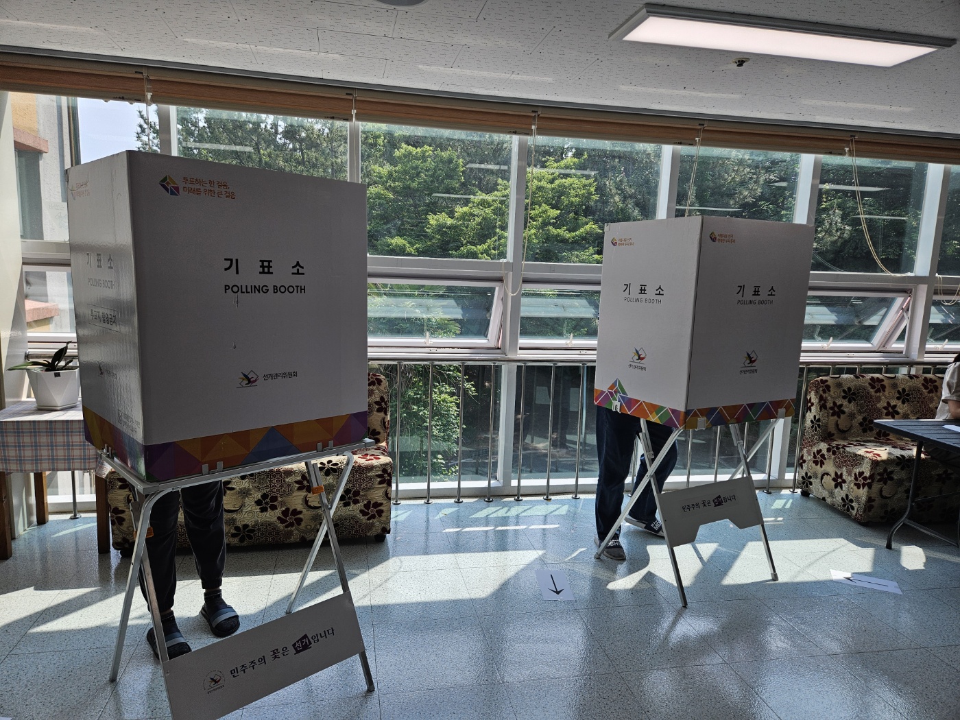 기표소 두곳의 정면이 보이고 있고 그 안에는 이용인 한명씩 각 기표소에 들어가 투표를 하고 있는 모습입니다. 