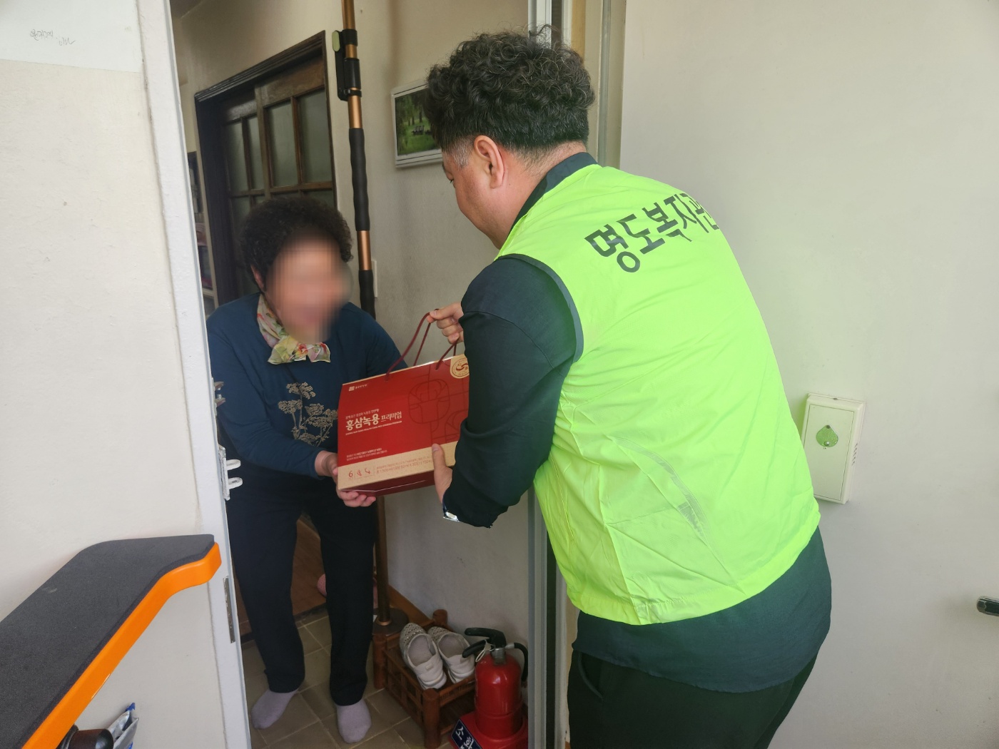 재가장애인 어르신 댁에 방문하여 건강식품을 전달하고 있는 담당 사회복지사의 모습입니다.