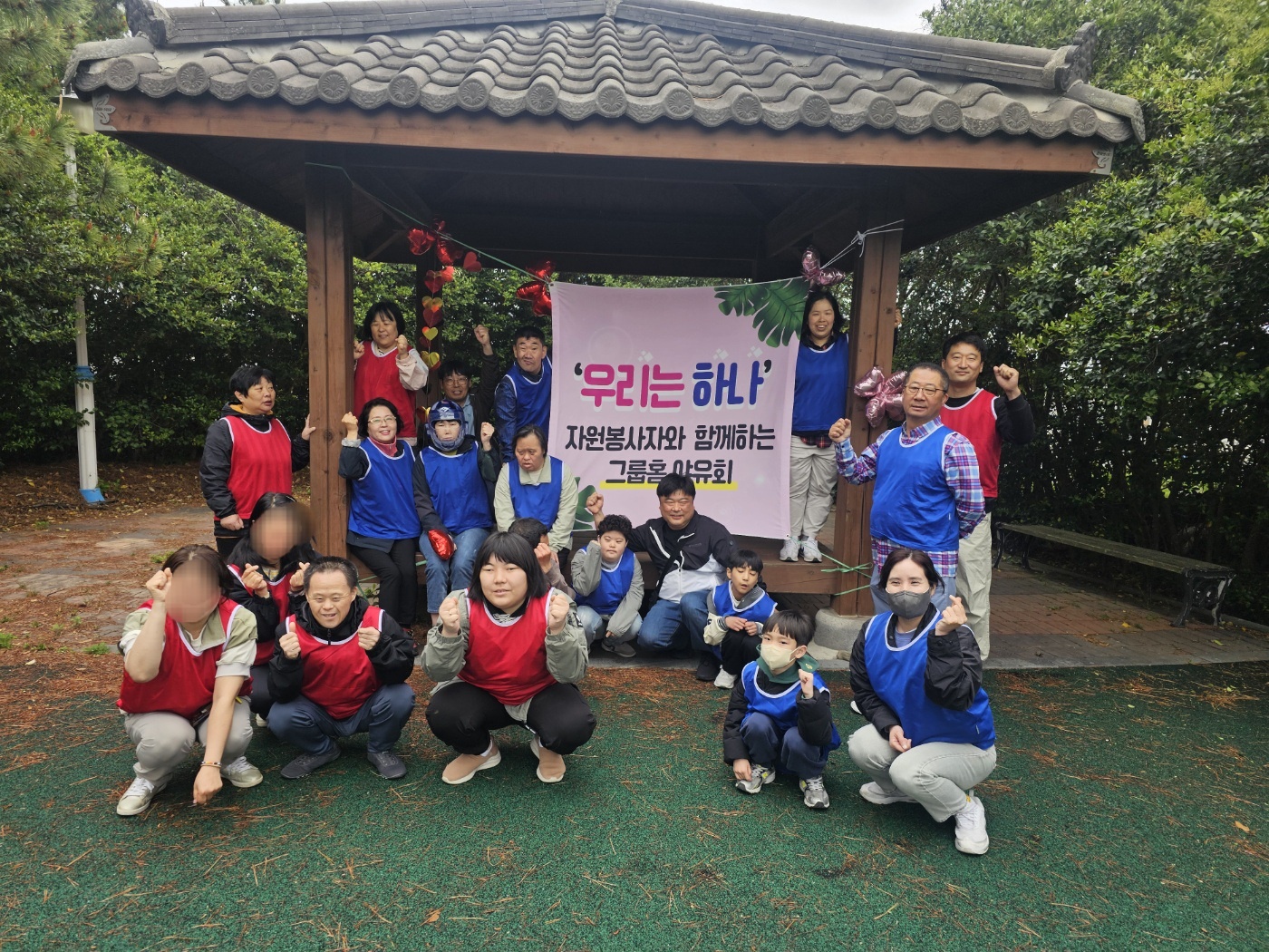 우리는 하나, 자원봉사자와 함께하는 야유회라는 현수막이 걸린 정자에 자원봉사자와 이용인들이 모두 앉아 함께 찍은 단체사진입니다. 