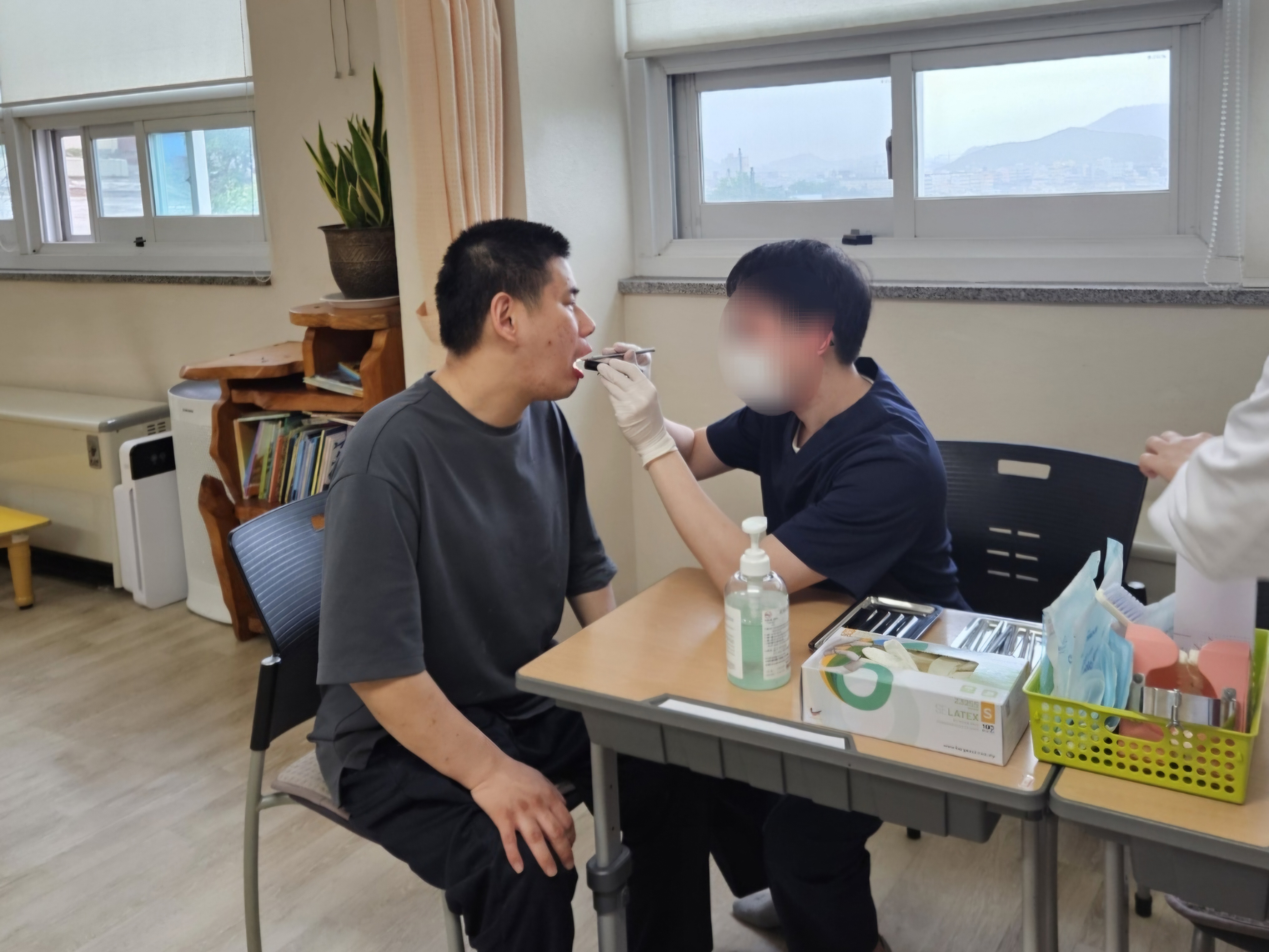 남성 이용인이 공중보건의 선생님께 구강검진을 받고 있는 사진입니다.