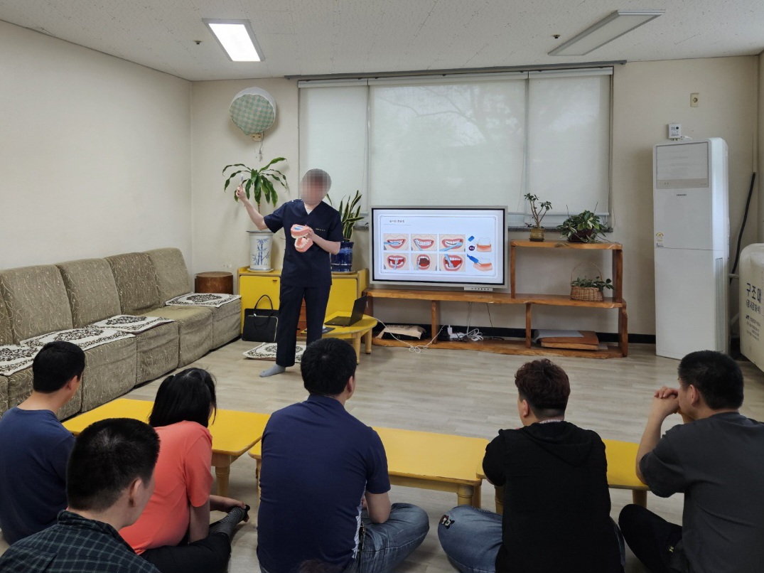 주간보호센터 이용인들이 책상 앞에 앉아 공중보건의 선생님께서 설명해주시는 '올바른 양치법'에 대하여 듣고 있는 모습입니다.