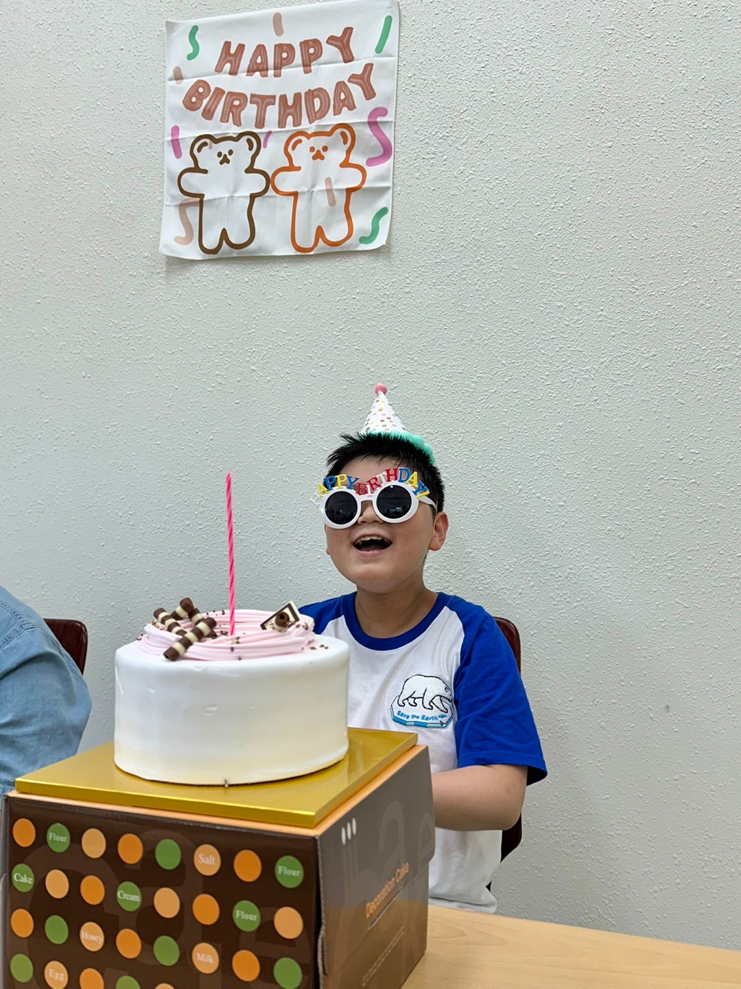 방과후교실 이용인이 케이크를 앞에 두고, 고깔모자를 쓴 채 밝게 웃고 있습니다. 