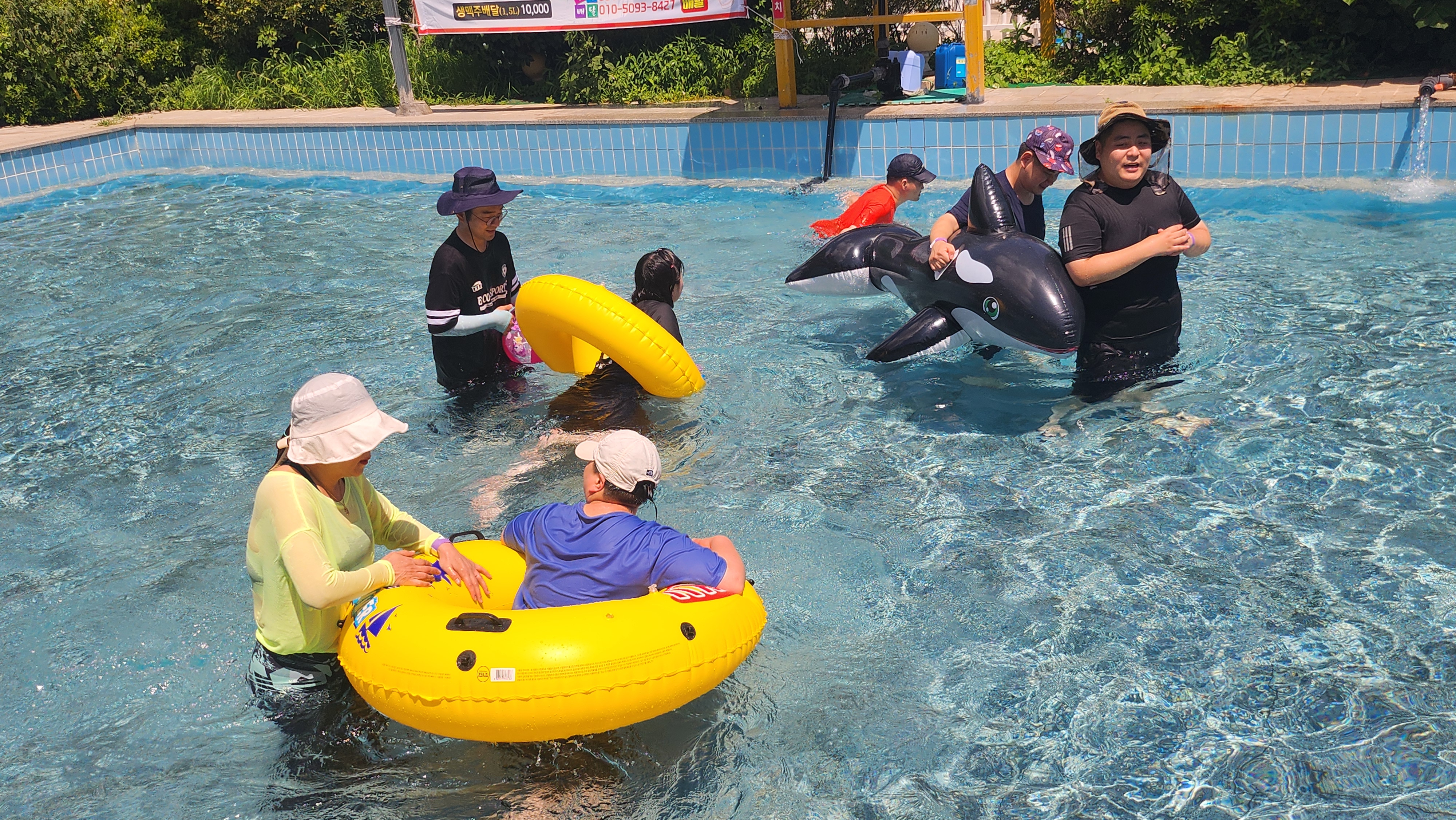 수영장에서 주간보호센터 이용인들과 교사가 튜브를 타고 함께 물놀이 하고 있는 사진입니다.