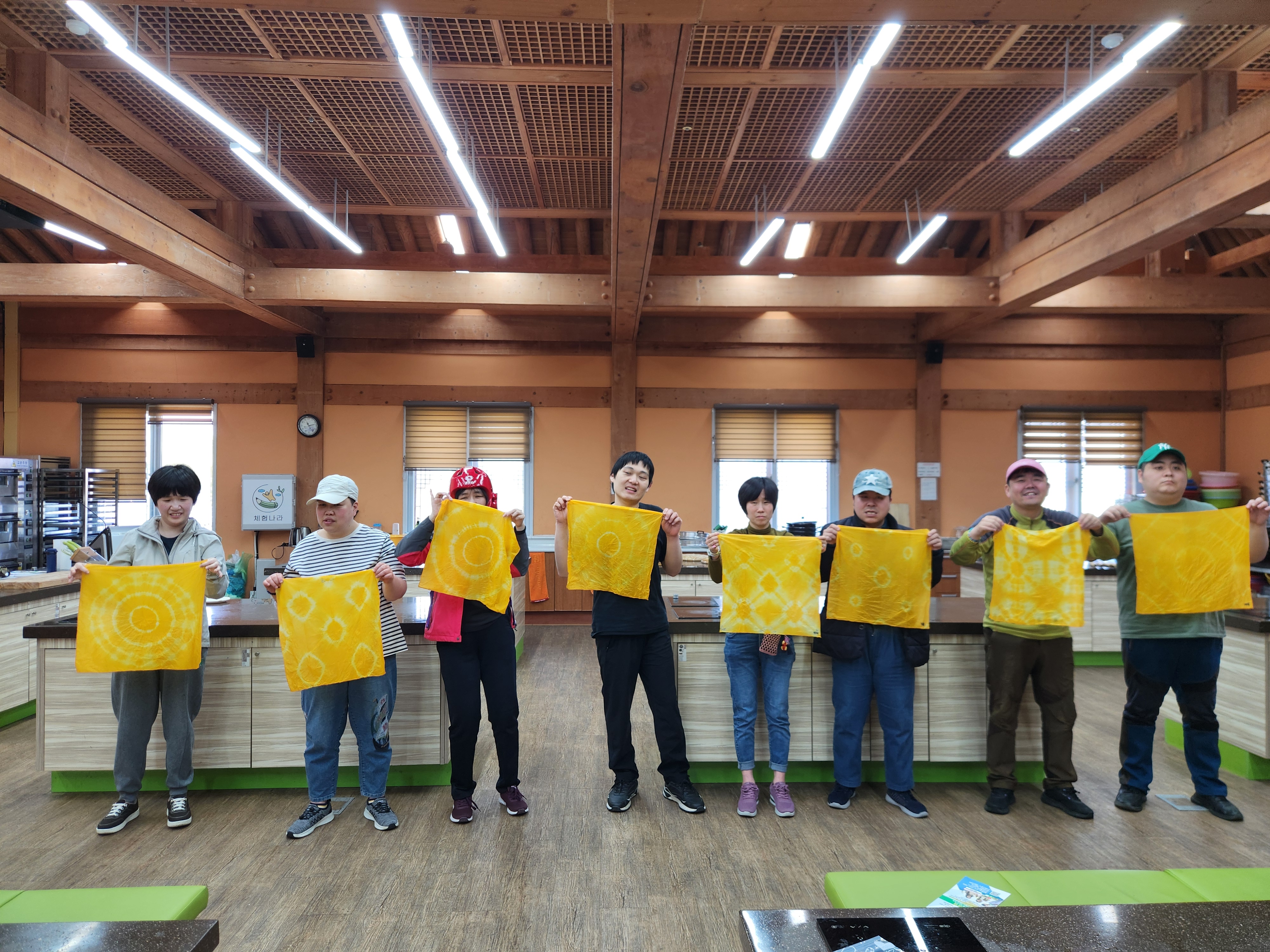 천연염색 손수건 만들기 체험을 한 후, 자신이 만든 가지각색 다른 모양의 손수건을 들고 한 줄로 서서 단체사진을 찍는 모습입니다.