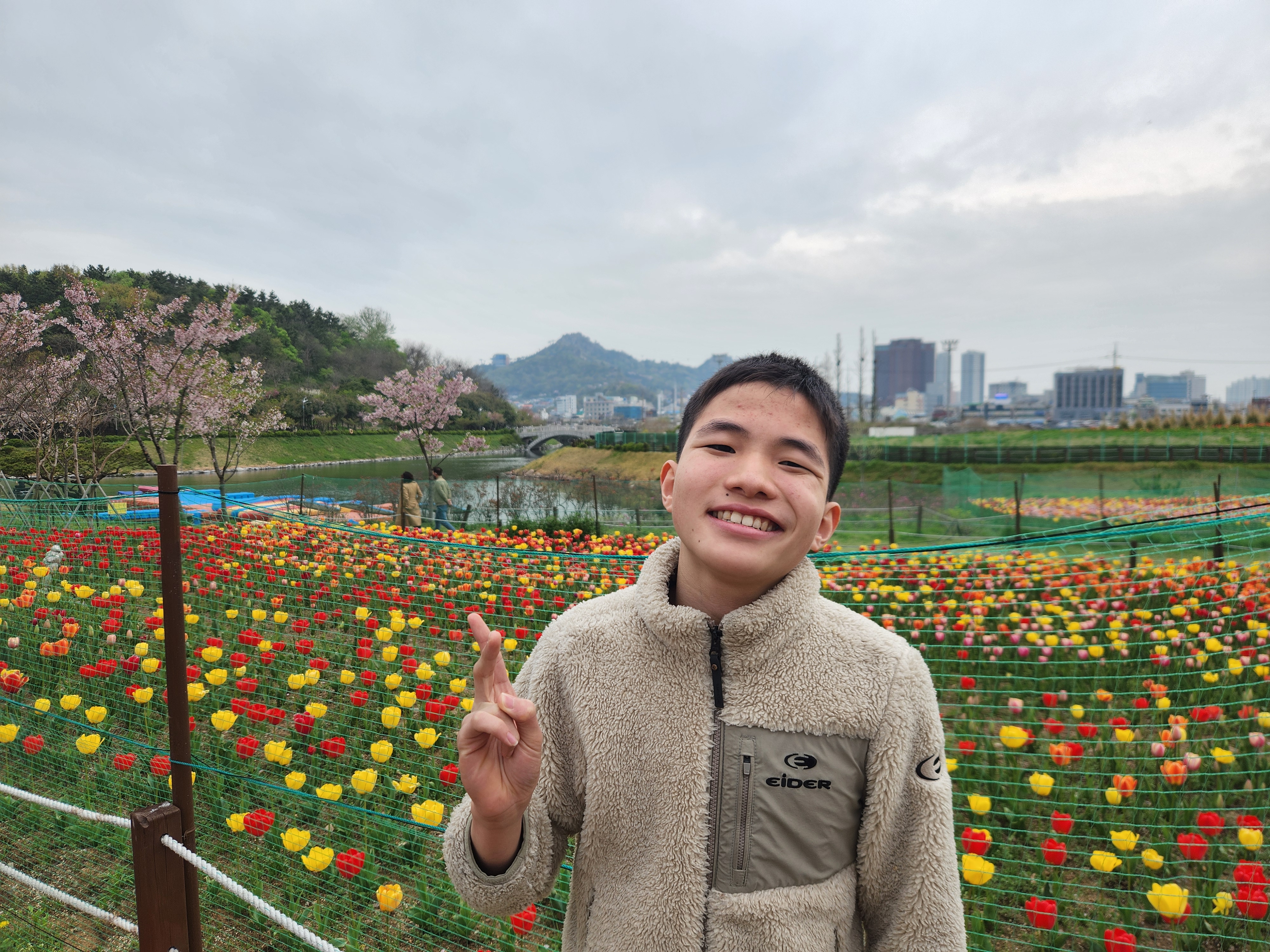 삼학도공원에 가득 핀 튤립을 배경으로 남자 이용인이 손으로 브이 포즈를 취하며 활짝 웃고 있는 모습입니다.